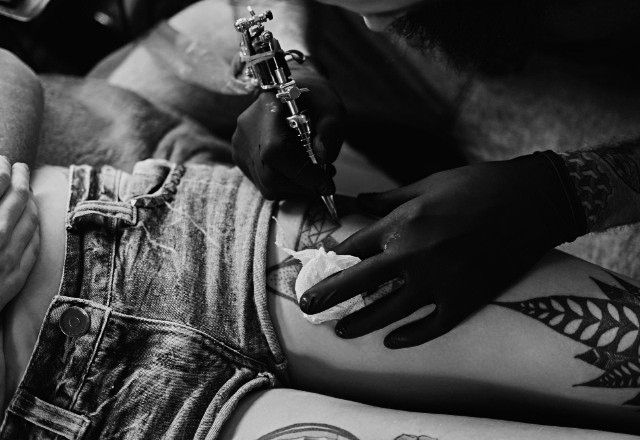 A client in short jeans shorts at a tattoo session in Auburn Tattoo shop